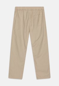 Beżowe spodnie o luźnym kroju z elastycznym pasem i jedną tylną kieszenią. Materiał wydaje się gładki o lekkiej teksturze.