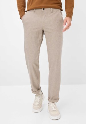 Beige, strukturierte Hosen mit schlankem Schnitt und umgekrempeltem Saum, ausgestattet mit einem Knopfverschluss und Seitentaschen, kombiniert mit hellen Sneakern.