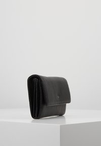 Portafoglio in pelle nera dalla trama sagomata con patta pieghevole e piccolo emblema metallico, posato su un piedistallo bianco su sfondo semplice.