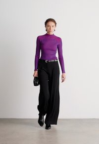 Camisola de manga longa roxa com textura, combinada com calças largas pretas de cintura alta. Os acessórios incluem uma pequena bolsa preta e botins pretos.