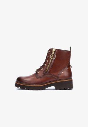 Bruine leren enkellaars met een ronde neus, zijrits, gouden hardware, veters en decoratieve studs aan de zijkant. Dikke rubberen zool.