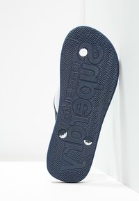 Suola di sandalini in gomma blu con motivo di grip testurizzato, che presenta il nome e il logo del marchio impressi. Due fori visibili vicino all'area del tallone.