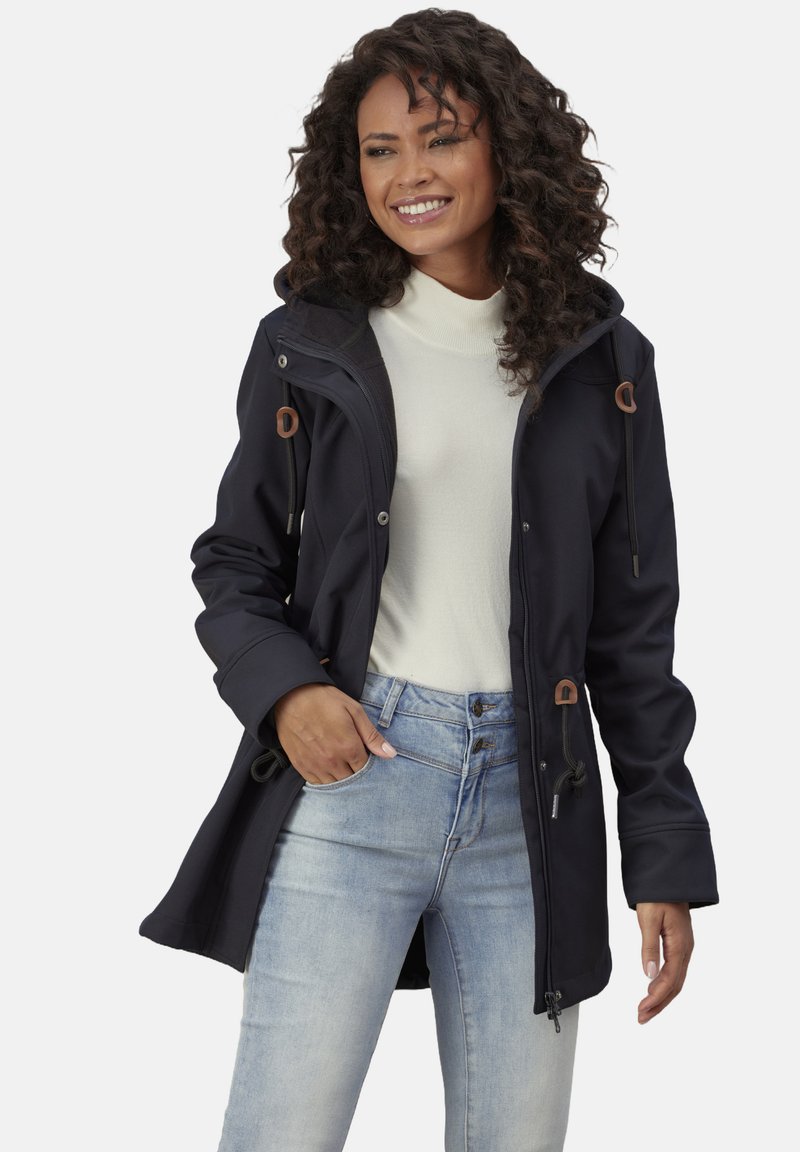 Navy softshell coat with a hood, drawstring details, and two front pockets, paired with a cream turtleneck and light blue jeans.
