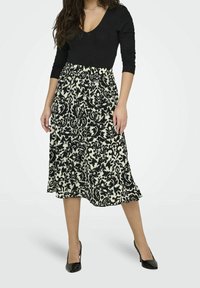 Mustapaita, jossa on pitkät hihat, yhdistetty polven pituiseen, virtaavaan hameeseen, jossa on musta-valkoinen kukkakuvio vaalealla taustalla.