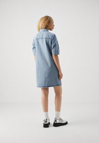 Šviesiai mėlyna džinsinė suknelė, trumpomis rankovėmis, su apykakle, kelių ilgio sijonu, su nuplyšusiomis kraštinėmis. Suknelei derinamos blizgios juodos platformos avalynės ir pilkos kojinės.