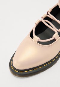 Sapato de couro rosa claro com biqueira arredondada, design de amarração e costura amarela contrastante ao longo da sola preta. Parte superior texturizada com recortes.