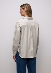Chemise rayée beige et blanc cassé, avec manches longues, col et coupe décontractée. Le dos présente une empiècement et un pli.