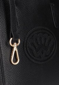 Zwarte leren tas met een gestructureerd oppervlak, voorzien van een opvallend rond reliëflogo en een goudkleurige metalen clip met een stevige bevestiging.