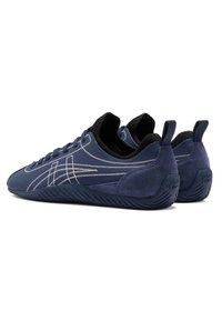 Navy blue sneakers made of suede and fabric, featuring white stitching accents, a textured sole, and a pull tab at the back for easy wear.