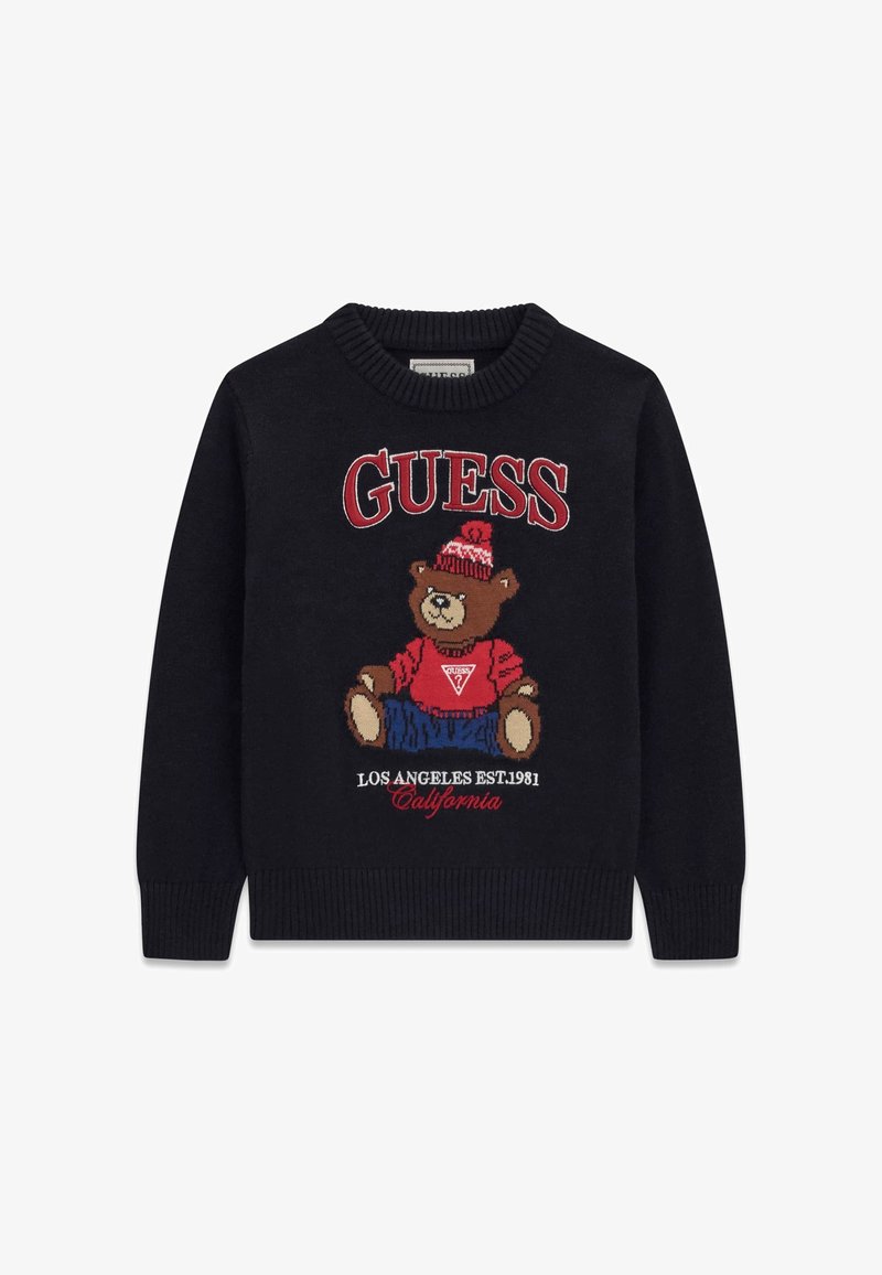 Pull noir avec un ours en peluche portant un chapeau rouge et un pull, pantalon bleu, texte "GUESS" au-dessus et "Los Angeles Est. 1981 California" en dessous.