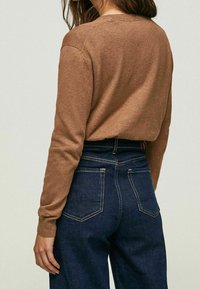 Brązowy sweter z dzianiny z długimi rękawami i okrągłym dekoltem, zestawiony z ciemnoniebieskimi jeansami o wysokim stanie z kontrastowymi detalami przeszyć.
