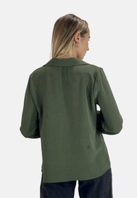 Groen collared shirt met een gestructureerde stof, lange mouwen en een rechte snit, van achteren getoond tegen een witte achtergrond.