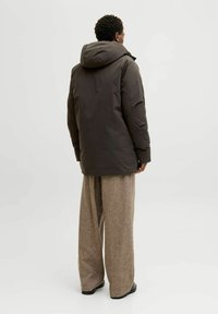 Tumši brūns pūkains jakas ar kapuci, ar plānu dizainu un teksturētu audumu, apvienots ar gaiši brūnām platām biksēm.