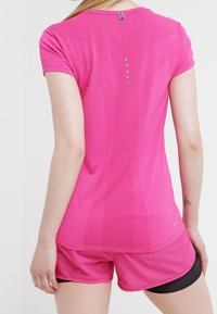 Fuchsia idrottströja med korta ärmar, strukturerad meshväv, med vertikala accentlinjer och en liten reflekterande logotyp på baksidan.