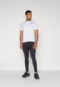 Mans aktivkläder set bestående av en vit kortärmad t-shirt och svarta åtsittande leggings med logotypen på vänster bröst och lår.
