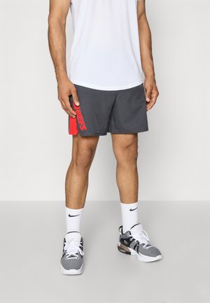 Shorts de sport gris avec un logo rouge sur le côté, associés à un t-shirt blanc, des chaussettes blanches et des baskets noir et blanc.