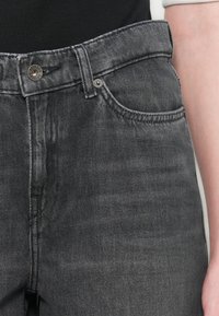 Close-up of high-waisted faded black denim jeans with visible button and front pocket, worn with a black top.