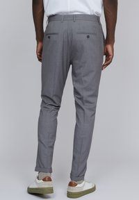 Pantalones a rayas grises con un corte entallado, que cuentan con dos bolsillos traseros y un dobladillo con vuelta. Combinados con zapatillas blancas y calcetines de textura visible.
