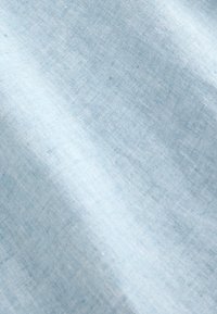 Gros plan d'un tissu tissé bleu clair avec une texture visible et des plis diagonaux subtils.