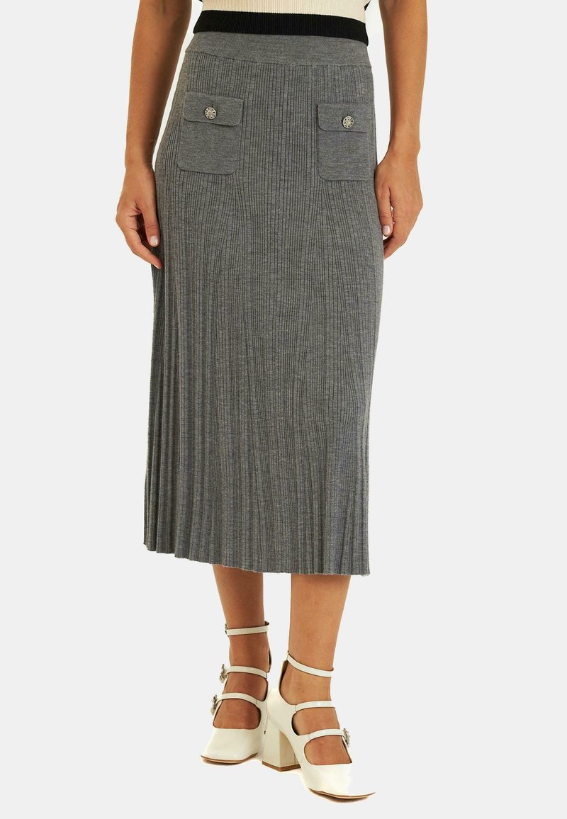 Jupe midi grise à côtes avec une taille ajustée, dotée de deux poches avant avec des boutons décoratifs. Portée avec des chaussures à talons carrés blanches.