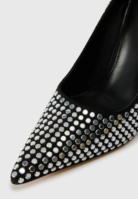 Must natuke musta stilettoga, millel on terav nina ja mis on kaetud hõbedaste peegli sarnaste nupukestega, mis on paigutatud ruudustikku. Sile sisetald.