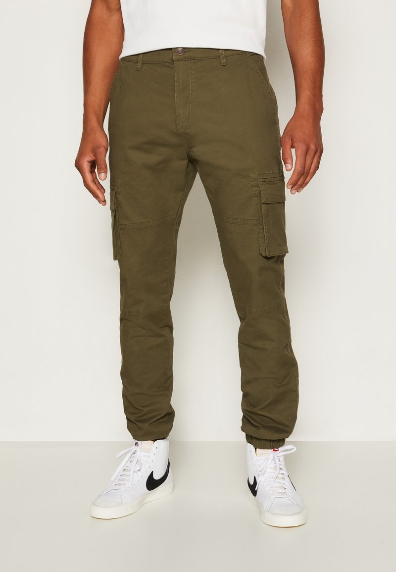 Pantalon cargo vert olive à coupe ajustée, doté de poches latérales et de poignets élastiques. Fabriqué en mélange de coton avec une texture lisse.
