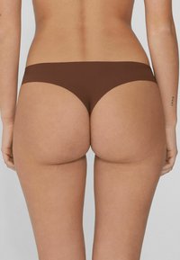 Brązowa bielizna bezszwowa, niskozabudowana, gładki materiał, minimalna osłona i zaokrąglony kształt wokół talii i bioder.