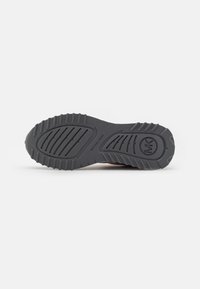 Semelle de chaussure en caoutchouc noir avec un motif de bande de roulement texturé, comportant des rainures et des crêtes pour une meilleure adhérence. Logo "Michael Kors" embossé sur la semelle.