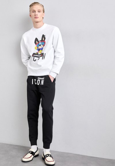 Hvid sweatshirt med grafikprint, sorte sweatpants med "ICON" tekst og kontrastfarvede sko. Glat tekstur, afslappet pasform og casual stil.