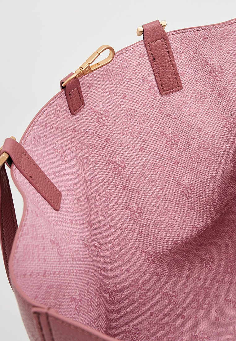 Bolsa de tela rosa con textura tejida, que presenta un ribete de cuero suave y herrajes en tono dorado. El interior muestra un patrón floral en relieve.