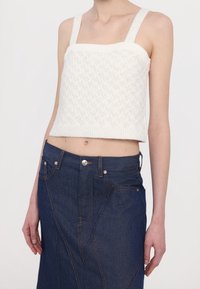 Witte gebreide crop top met gestructureerde banden en textuurpatroon, gecombineerd met een donkere denim rok met contrasterende stiksels en knopdetails.