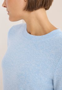Maglione azzurro chiaro con scollo a girocollo, realizzato in tessuto testurizzato. Presenta una vestibilità leggermente ampia e un aspetto morbido.