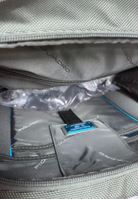 Interno della borsa grigia con più scomparti. Tessuto liscio con dettagli blu e marchio. Chiusura con cerniera per la conservazione.