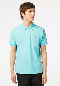 Polo shirt azzurro chiaro in cotone con colletto classico, due bottoni, maniche corte e logo ricamato verde sul petto.