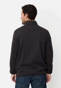 Dunkelgrauer Fleece-Pullover mit hohem Kragen, strukturierter Oberfläche und geradem Schnitt. Verfügt über eine dezente Nahtdetail über den Schultern.