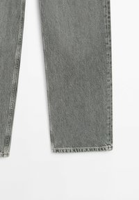 Jambes de jeans en denim gris avec des coutures visibles et un ourlet droit sur fond blanc.