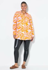 Chemise à manches longues avec un motif rayé tigre orange et rose, associée à des leggings en simili cuir noir et des chaussures à enfiler marron.