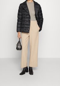 Černá péřová bunda s dvojitým zapínáním, béžové široké kalhoty, černé kotníkové boty a malá černá kabelka.