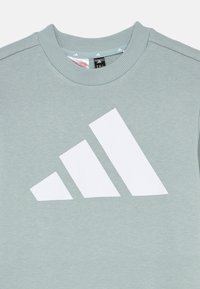 Jasnozielona bluza z białym logo z trzema paskami. Wykonana z miękkiego materiału, ze ściąganym dekoltem i standardowym krojem.