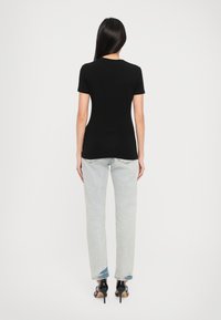 Melnas, pieguļošas T-krekls, izgatavots no mīksta materiāla, kombinēts ar gaiši izbalējušām taisna griezuma džinsiem. Ievērojams elements ir melnas augstpapēžu kurpes.