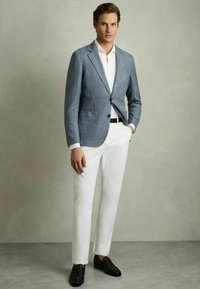 Un sacou ușor, în carouri albastre și albe, purtat peste o cămașă albă, asortat cu pantaloni strâmți albi și mocasini negri. Textură netedă și croială ajustată.
