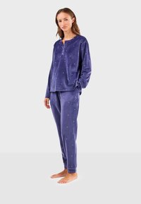 Ensemble de pyjama en velours violet comprenant un haut à manches longues avec un col à boutons et un pantalon assorti orné de petits pois blancs.