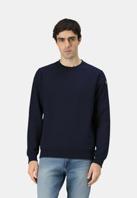 Felpa blu navy in tessuto morbido, con scollo rotondo e polsini a costine. Indossata da un modello su sfondo semplice.