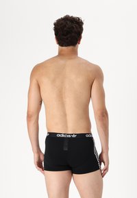 Svarte boksershorts med hvit Adidas-logo på midjebåndet og tre hvite striper på sidene, laget av elastisk materiale.