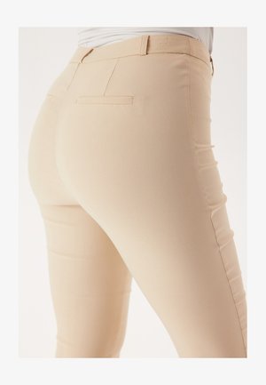 Light beige fitted pants with a smooth texture, featuring two back pockets and subtle stitching details. Mid-rise waist with belt loops.