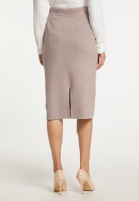 Strick-Bleistiftrock in Hellbeige mit hohem Bund und einem Schlitz hinten, kombiniert mit hautfarbenen High Heels. Glatte Textur und figurbetonte Passform.