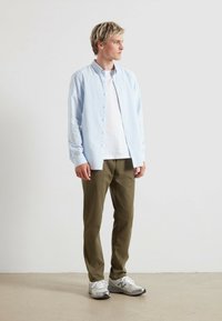Jasnoniebieska koszula w paski noszona na białym T-shircie, w połączeniu z oliwkowymi spodniami i szarymi sneakersami. Prosty design, swobodny fason.