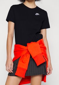 Person som bär en svart Nike-t-shirt, svart randig kjol och en lysande röd sweatshirt knuten runt midjan.