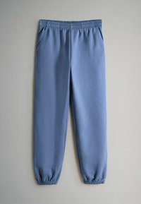 Svetlomodré tepláky s elastickým pásom, bočnými vreckami a zúženými manžetami. Látka pôsobí mäkko a hladko.