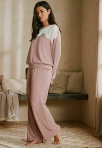 Gaiši rozā mājas apģ�ērbu komplekts ar brīva piegriezuma džemperi, kam ir kontrastējoša gaiši zila augšējā daļa, un atbilstošām platajiem biksēm ar rievotu tekstūru.